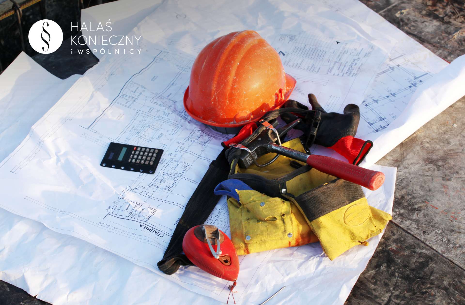Ekwipunek budowlańca, kask, narzędzia, rękawice leżące na planach zabudowy